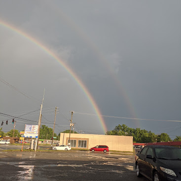 A double rainbow over the Dino Food Mart building and parking lot after a storm