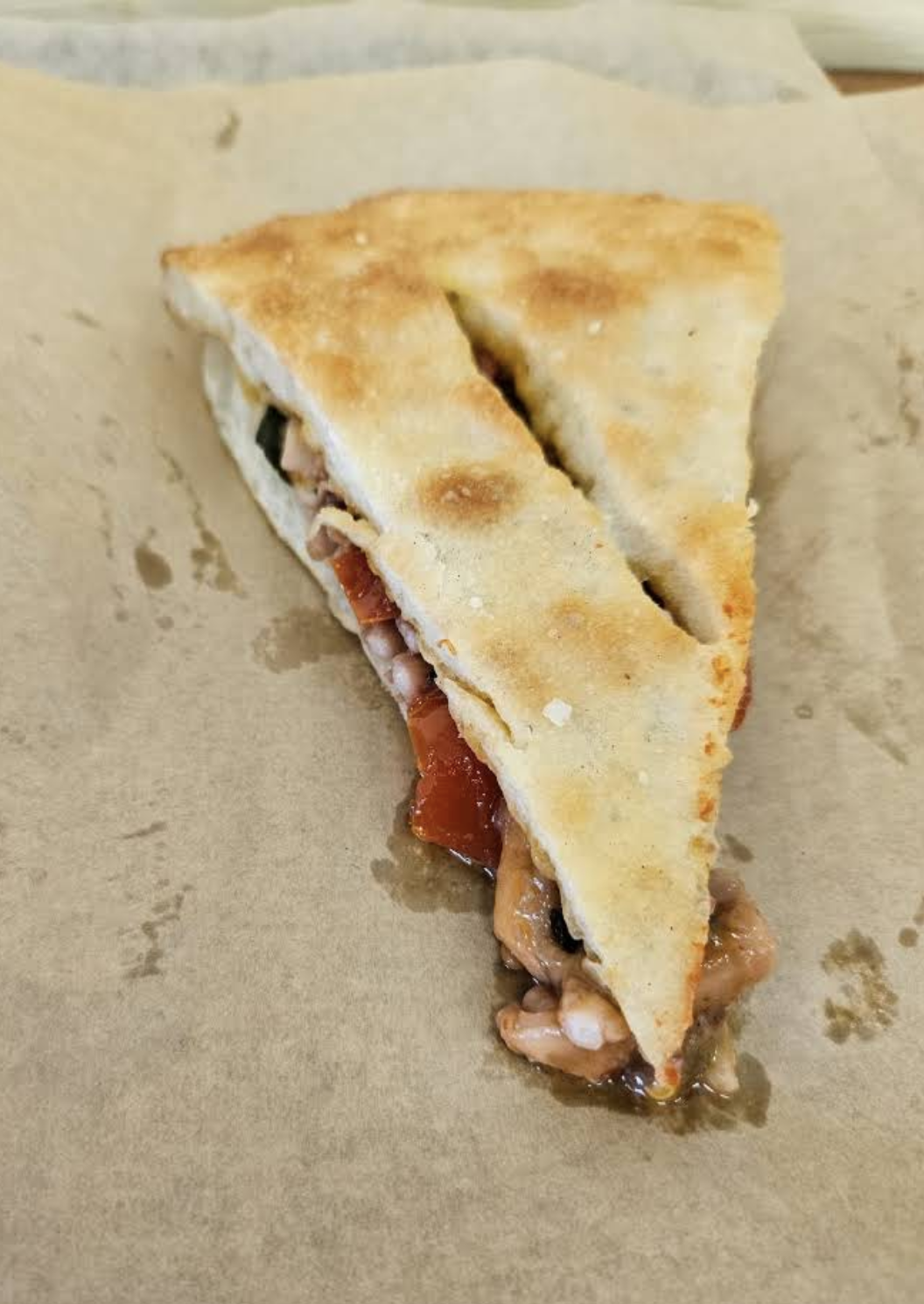 A folded slice of pizza filled with tomato and octopus, on baking paper