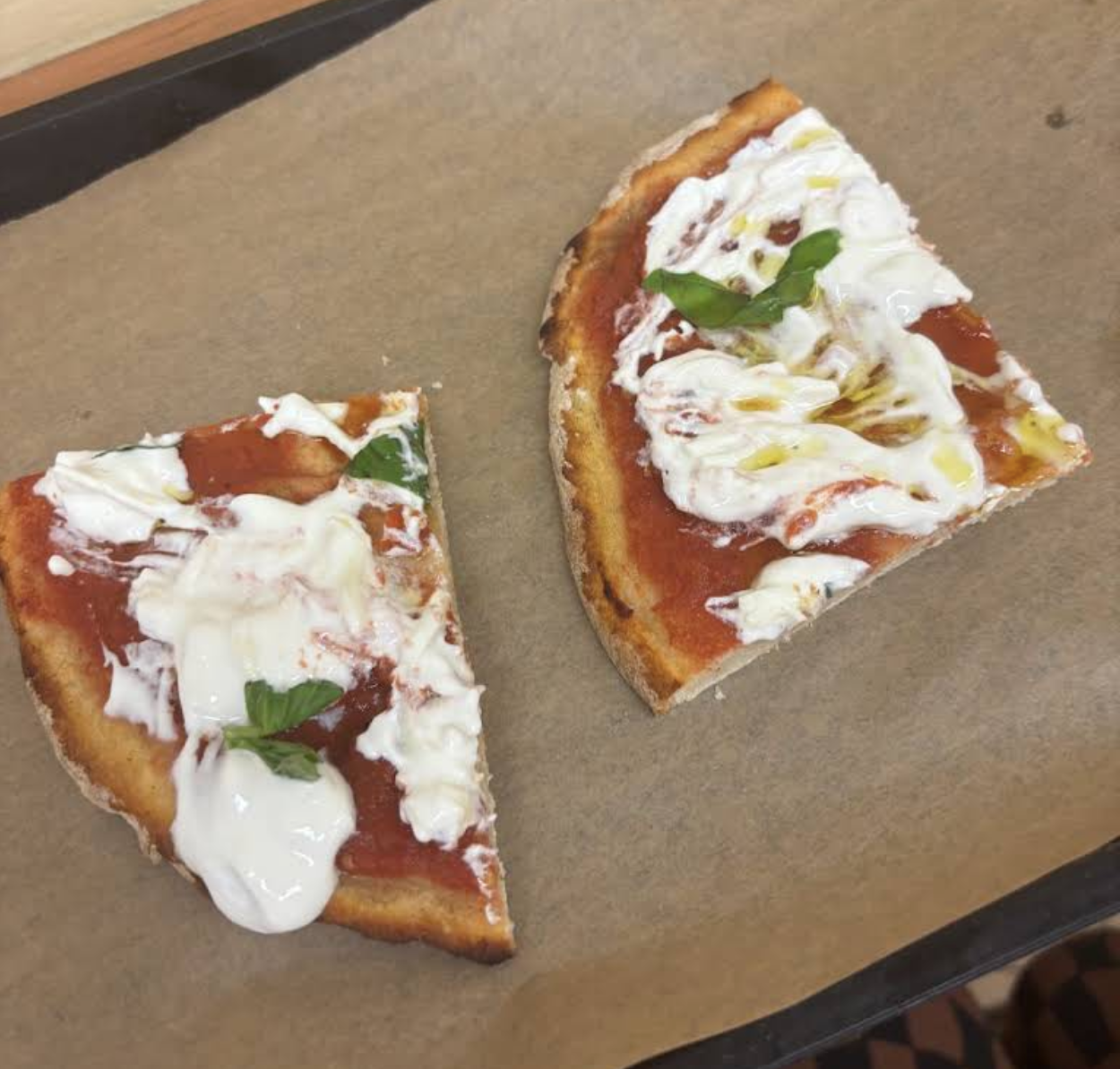 Two pieces of pizza with tomato, fresh cream cheese, basil and olive oil