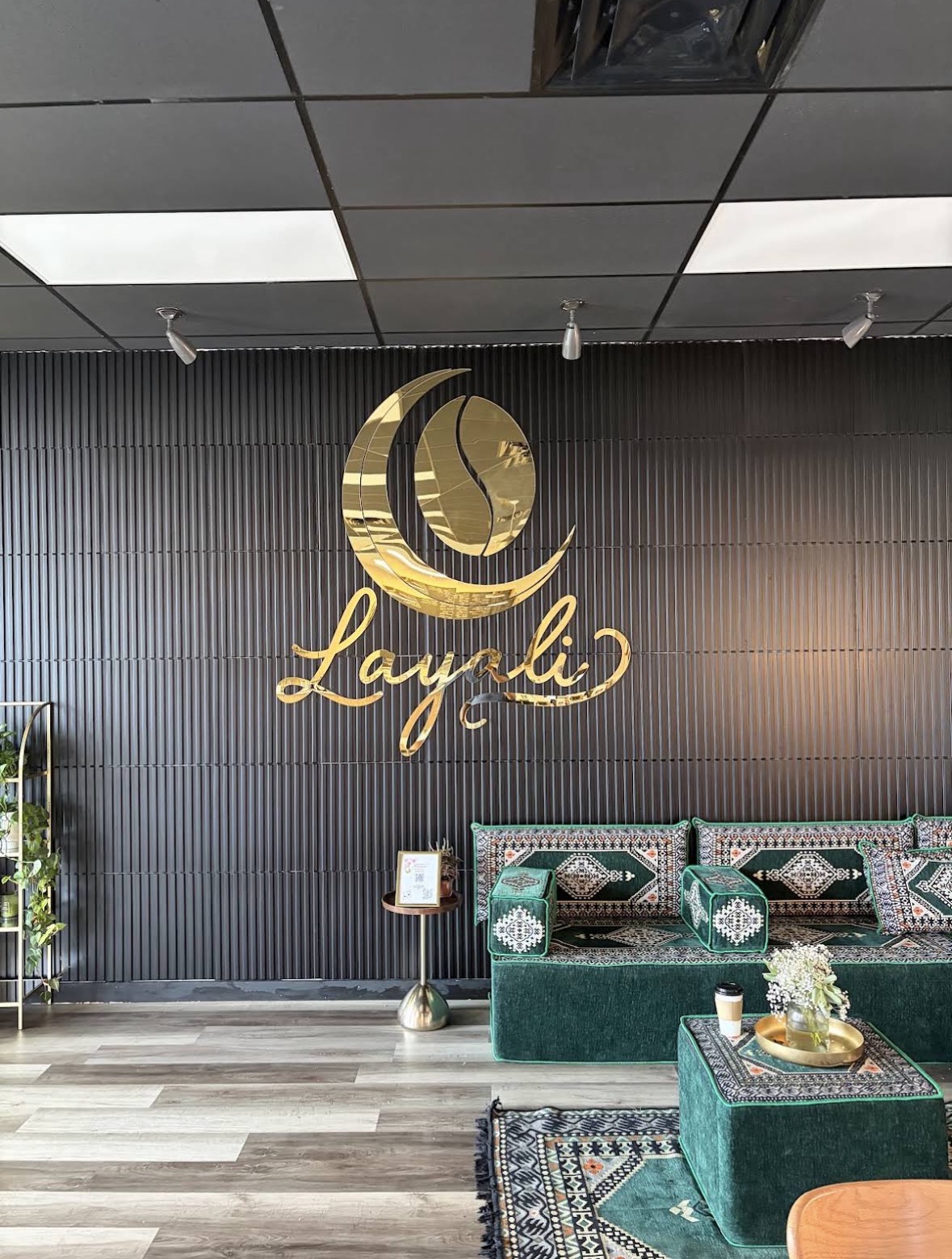 The gold Layali logo on a dark wall above green patterned seating