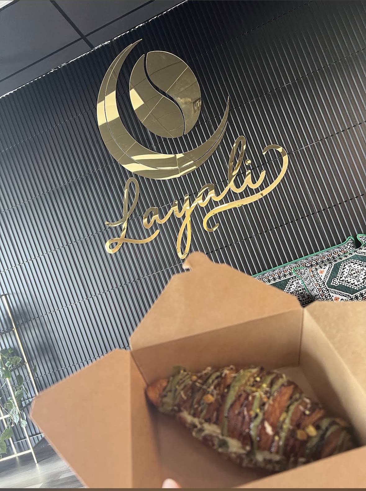 A Dubai pistachio croissant with green pistachio drizzle in a paper box, under the gold Layali logo